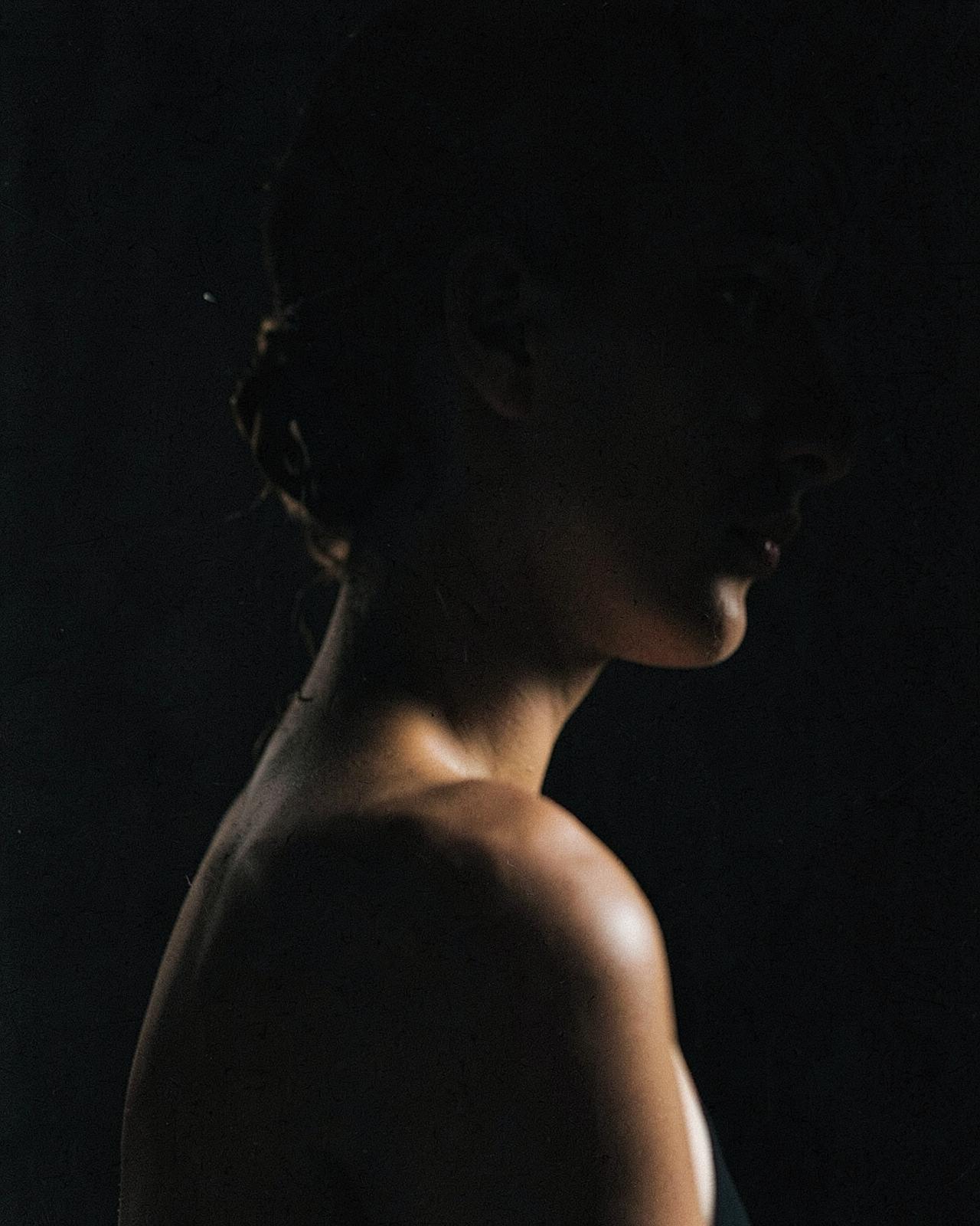 A bare shoulder and jawline in deep shadow, the face turned away