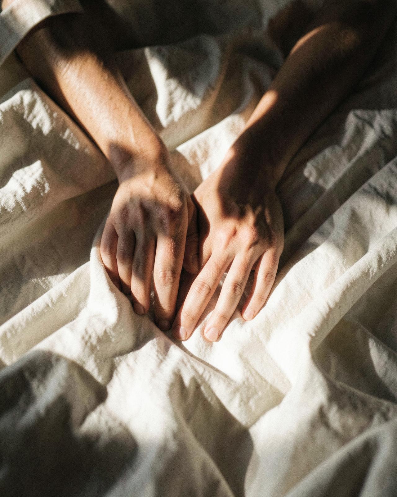 Hands resting on rumpled ivory linen in warm sunlight