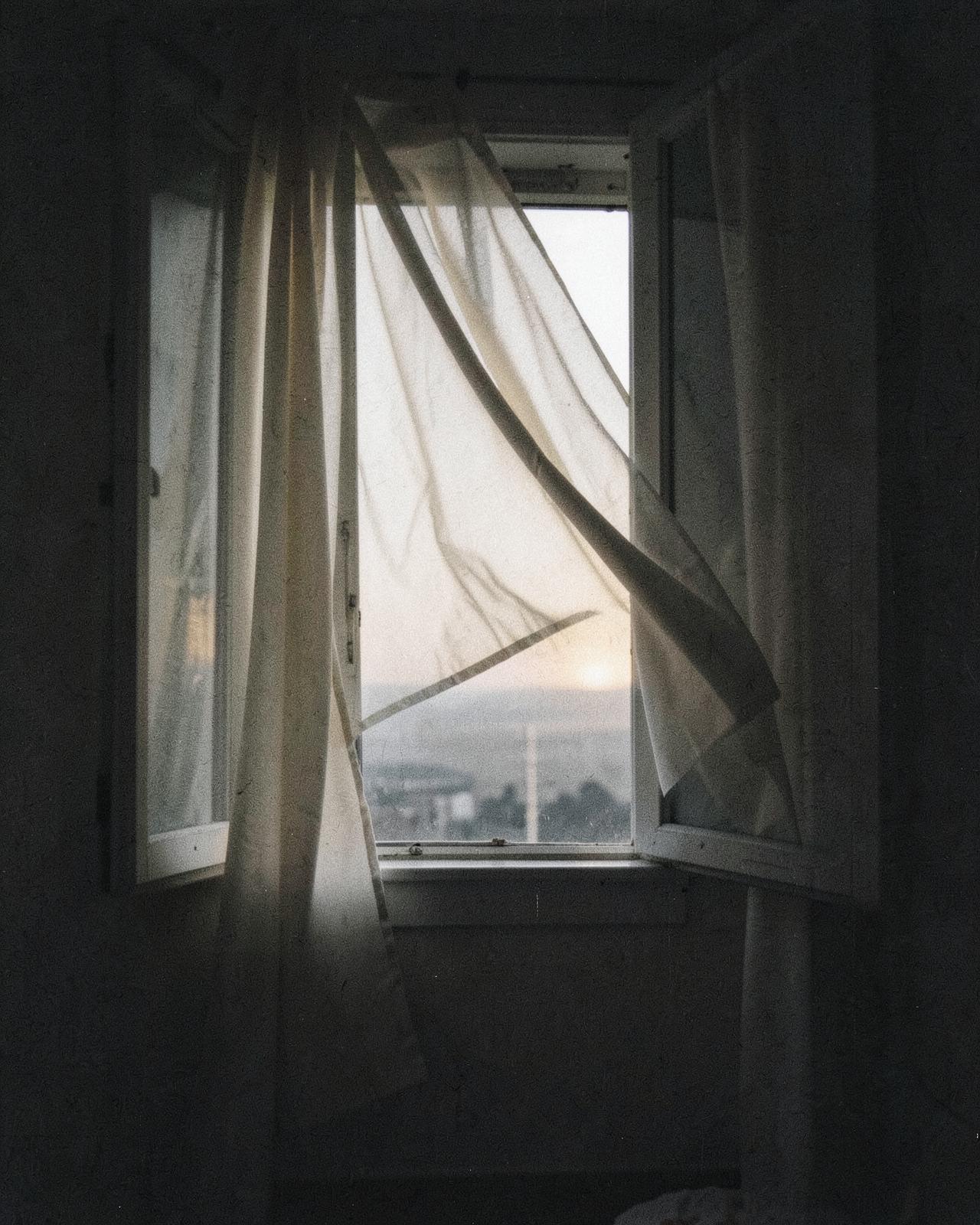 A sheer curtain lifting at an open window with faint light beyond
